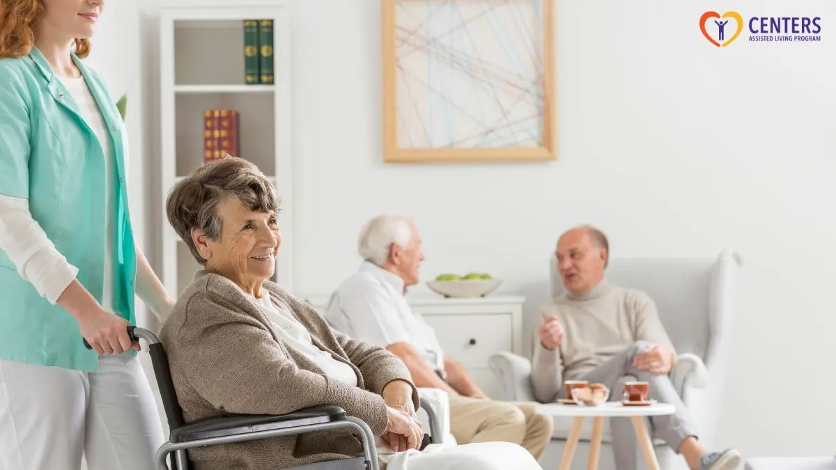 caregiver-pushing-senior-in-wheelchair-in-assisted-living-lounge